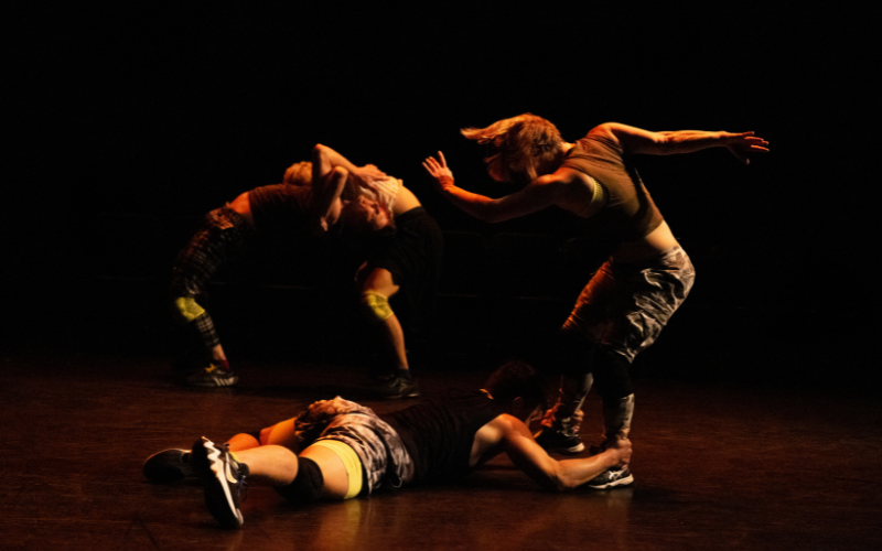 Four dancers - two standing and two on the ground with their arms around the standing dancers legs