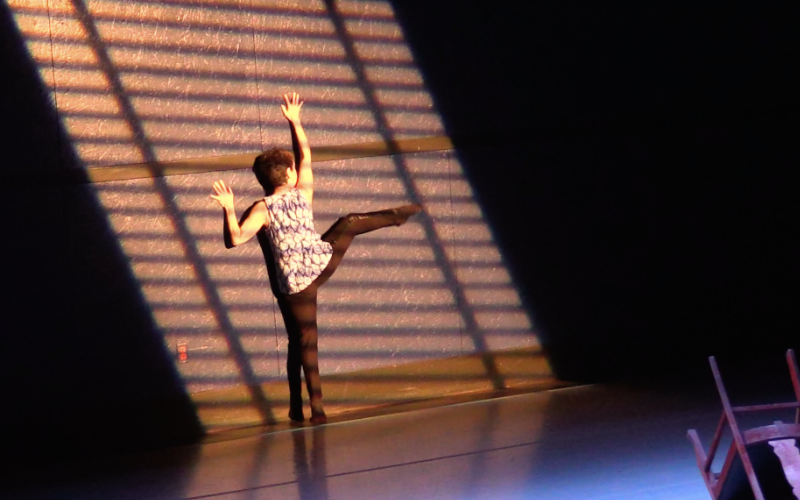 A performer against a wall with arms outstretched and leg up