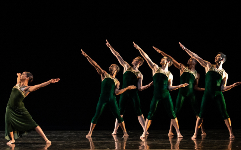 Several dancers on stage motioning towards a lead dancer doing a different movement than the rest