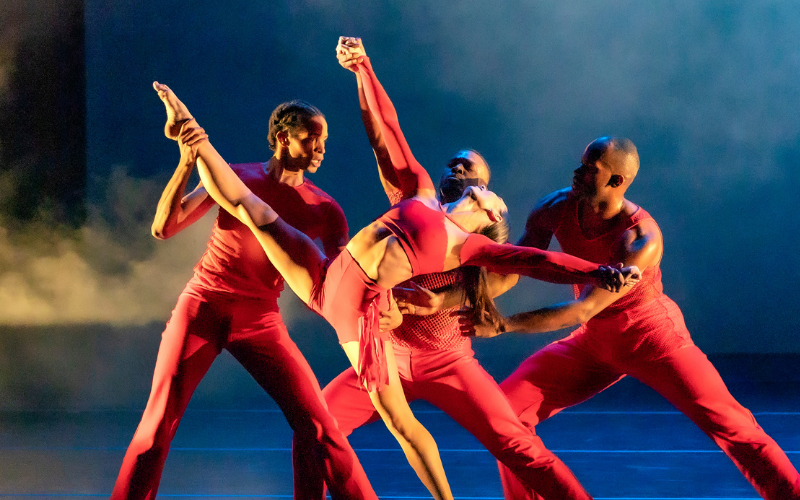 Four dancers wearing red performing on a smoky stage