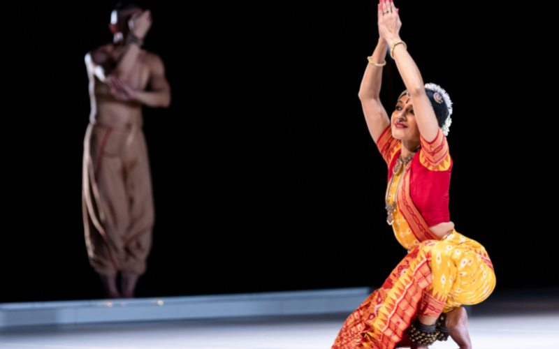 A dancer kneels on the ground with hands in praying position pointing upward