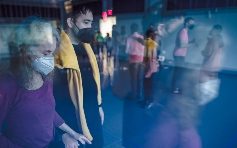Multiple exposure image of Co-Director Davian Robinson in silhouette sitting on the dance studio floor in front of large windows.