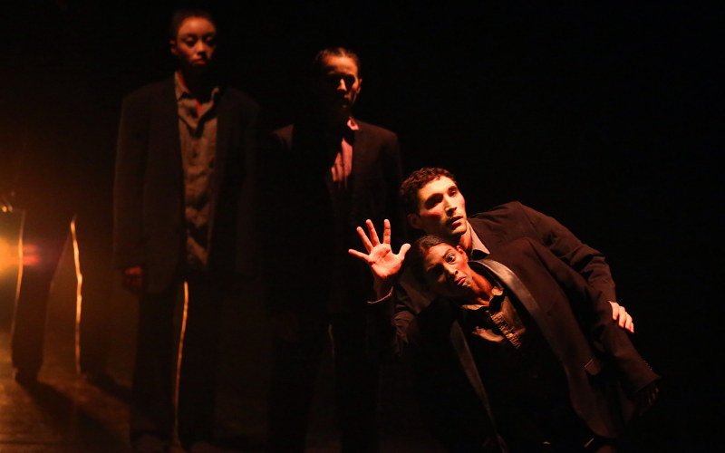 Two dancers pose closely in similar outfits while two dancers look on in the background