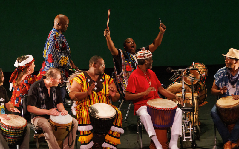 7 drummers sit together on stage.