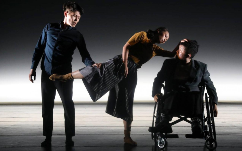 3 dancers on stage, induing one standing, one leaning, and one sitting in a wheelchair.