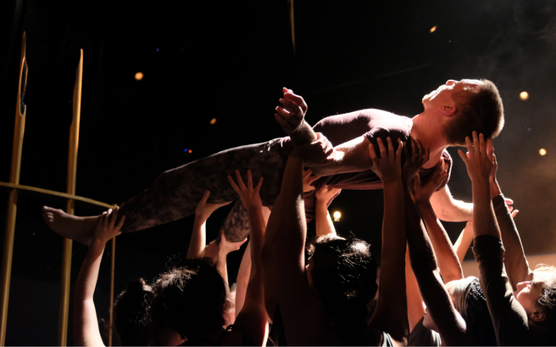 A dancer is lifted on their back by the arms of others.