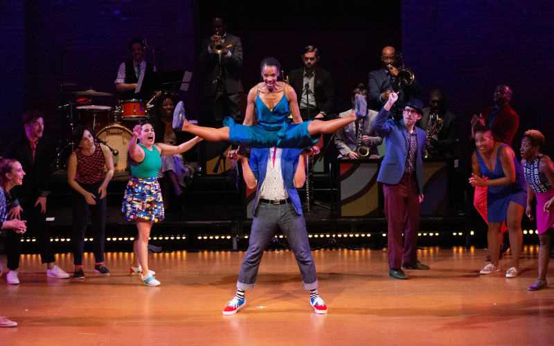 A dance lifts another into the air as her kegs extend to the side in a middle split.